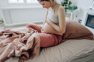 Schwangere Frau sitzt im Bett und hält ihren Bauch