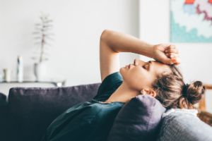 Erschöpfte Frau liegt mit geschlossenen Augen auf dem Sofa.