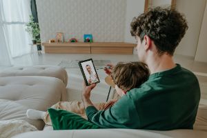 Eine Frau sitz in ihrem Wohnzimmer mit einer Tasse in der Hand auf dem Fußboden und schaut lachend auf ihr Smartphone.