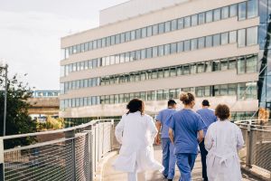 Medizinisches Fachpersonal läuft über eine Brücke auf ein Krankenhaus zu.