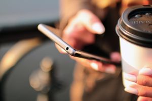 Person hält ein Smartphone und einen Kaffeebecher in der Hand.