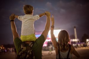 Vater mit Kind auf den Schultern tanzt abends mit seiner Partnerin auf einem Festival.