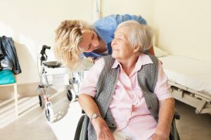 Pflegerin spricht mit alter Frau im Rollstuhl.