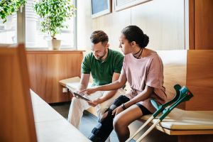 Krankengeldanspruch nach 6 Wochen: Ein junger Mann mit Gipsbein sitzt auf dem Sofa und schaut auf sein Tablet.