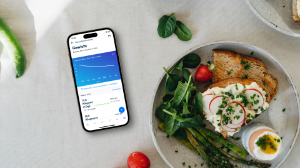 Ein Handy mit dem Gesundheitstracking von Gro Health liegt neben einem Teller mit gesundem Essen.