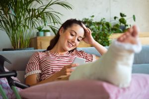 Eine junge Frau sitzt auf dem Sofa und hat ein gebrochenes Bein.