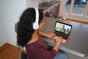 Eine junge Frau sitzt zuhause am Tisch und erhält über ihr Laptop eine Online-Beratung.