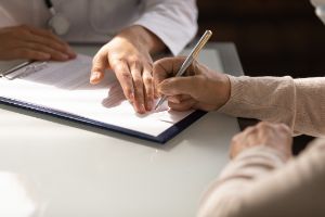 Eine Patientin unterschreibt ein Dokument beim Arzt.