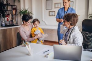 Ein kleines Mädchen und ihre Mutter sitzen mit einer Ärztin und einer Krankenschwester zusammen.