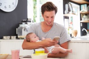 Ein Mann hält ein Baby auf dem Arm und bedient ein Smartphone.