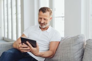 Ein Mann sitzt mit seinem Tablet auf einem Sofa.