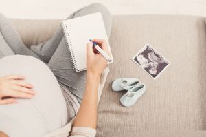 Schwangere sitzt auf dem Boden mit einem Zettel und Stift in der Hand