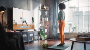 Eine junge Frau macht ein Workout zuhause vor ihrem Fernseher.