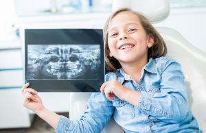 Glückliches junges Mädchen neben Röntgenaufnahme ihres Kiefers.