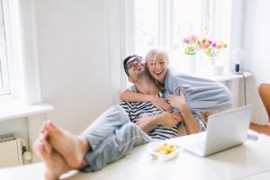 Pärchen umarmt sich zufrieden am Esstisch vor einem Laptop.