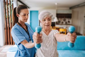 Eine ältere Frau macht Übungen mit Hanteln mit einer Physiotherapeutin. 