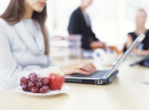 Obstteller steht neben einer Frau mit Laptop auf dem Schreibtisch.