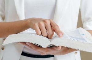 Eine Frau hält ein aufgeschlagenes Buch in den Händen und zeigt mit einem Finger auf eine Stelle im Buch.