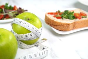 Auf einem Tisch liegt ein Apfel, um den ein Maßband gebunden ist, sowie weitere gesunde Lebensmittel.