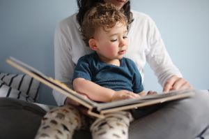 Ein kleiner Junge sitzt auf dem Schoß seiner Mutter und schaut in ein Buch.