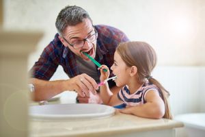 Vater und Tochter putzen die Zähne am Waschbecken