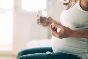 Eine schwangere Frau nimmt eine Tablette mit Hilfe eines Glases Wasser ein