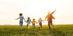 Eine Familie mit drei Kindern läuft im Sommerabendlicht über eine Wiese