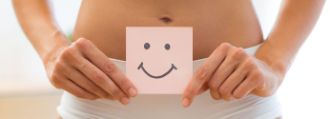 Eine junge Frau hält ein Stück Papier mit einem Smiley drauf über ihren Bauch.