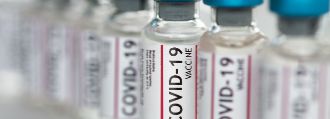 Mehrere Flaschen Covid-19-Impfstoff stehen auf einem Fließband.