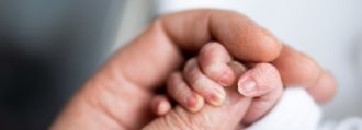 Eine erwachsene Hand hält die Hand eines Neugeborenen.