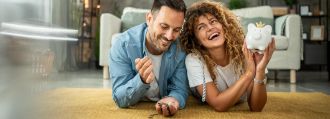 Ein paar liegt auf dem Boden mit Geld und einem Sparschwein in der Hand und freut sich.