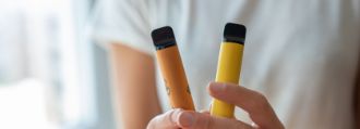 Eine Person hält zwei gelbe E-Zigaretten in den Händen.