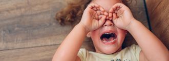 Ein Kind liegt auf auf dem Boden, hat die Hände vor den Augen und schreit.