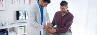 Ein Patient sitzt auf einer Behandlungsliege und lässt sein Knie von einem Arzt anschauen.