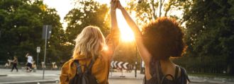 Zwei Mädchen halten Ihre Hände zu einem ausgetrecktem High five verbunden in die Abendsonne
