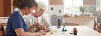 Alte Frau sitzt mit jüngerer Frau gemeinsam vor einem Tablet am Tisch