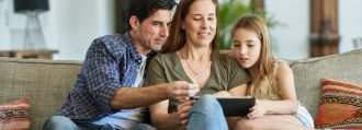 Vater, Mutter und Tochter sitzen auf dem Sofa und schauen auf ein Tablet