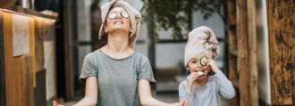 Mutter und Tochter meditieren mit einer Gesichtsmaske und Gurken.