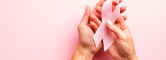 Zwei Hände halten die rosa Brustkrebs-Schleife in der Hand.
