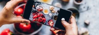 Zwei Hände halten ein Smartphones, durch dessen Kamera man verschiedene Lebensmittel sieht.