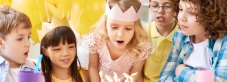 Maedchen pustet bei Kindergeburtstag Kerzen auf Kuchen aus