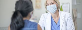 Eine Ärztin mit Mund-Nasen-Bedeckung berät eine Frau.