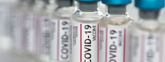 Mehrere Flaschen Covid-19-Impfstoff stehen auf einem Fließband.
