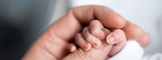 Eine erwachsene Hand hält die Hand eines Neugeborenen.