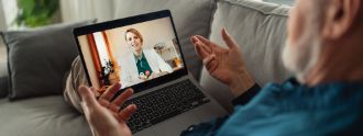 Älterer Mann schaut auf Tablet, macht Video-Call mit Ärztin. 