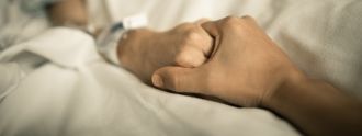 Die Hand einer jungen Person hält die Hand einer alten Person, die in einem Krankenhausbett liegt