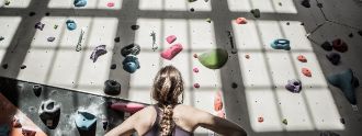 Eine Frau steht vor einer Boulderwand und schaut hoch.