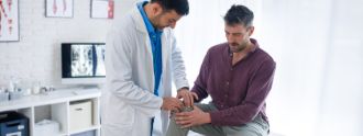 Ein Patient sitzt auf einer Behandlungsliege und lässt sein Knie von einem Arzt anschauen.