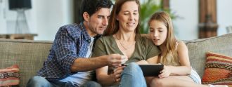 Vater, Mutter und Tochter sitzen auf dem Sofa und schauen auf ein Tablet