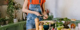 Eine junge Frau steht in der Küche und kocht eine gesunde Mahlzeit.